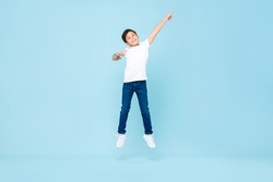 Cute Asian mixed race boy jumping with hand pointing up in isolated light blue color studio background