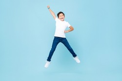 Cheerful Asian mixed race boy jumping and raising hand up in isolated light blue color studio background