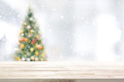 Wood table top on blur Christmas tree and white bokeh in snowfall background