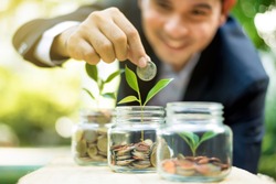 Businessman putting coin into the glass jar with young plant, demonstrating financial growth through saving plans and investment schemes