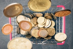 Shopping basket with falling Euro coins over grey stone background. Top view. Сonsumer budget and purchasing capacity concept