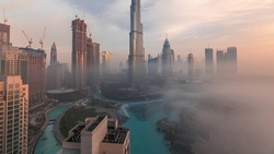 Aerial panoramic view of Dubai city early morning during fog timelapse. Sunrise at futuristic city skyline with skyscrapers and towers from above. Sun reflected from glass surface