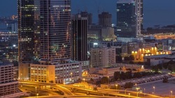 Office buildings in Dubai Internet City and Media City district aerial night to day transition timelapse. Traffic on junction and skyscrapers with sunrise and sun reflected from glass