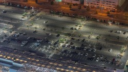 Big parking lot near mall crowded by many cars night timelapse aerial view. Vehicles moves in and out