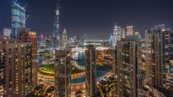 Dubai Downtown cityscape with tallest skyscrapers around fountain aerial night timelapse. Construction site of new towers and busy roads with traffic from above