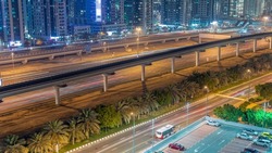 Highway near Dubai marina skyscrapers night timelapse. Aerial view from JLT district to apartment buildings, hotels and office towers with metro line and parking lot