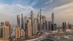 Skyscrapers of Dubai Marina with illuminated highest residential buildings morning timelapse. Traffic on highway intersection. Aerial top view from JLT district during sunrise
