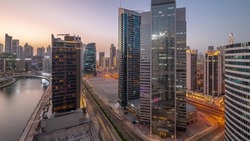Cityscape of skyscrapers in Dubai Business Bay and downtown with water canal aerial day to night transition. Modern skyline with towers and waterfront after sunset. A center of international business