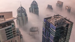 Towers covered by rare early morning winter fog above the Dubai Marina skyline and skyscrapers rooftops aerial timelapse. Top view from above clouds. Dubai, UAE