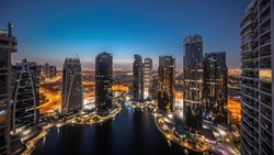 Tall residential buildings panorama at JLT district aerial night to day transition timelapse, part of the Dubai multi commodities centre mixed-use district. Illuminated towers and skyscrapers