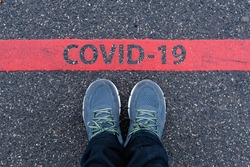 man in sneakers standing next to a red line with text COVID-19, restriction or safety warning concept