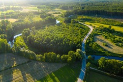 Latvian rural landscape with a winding river, forests and country roads at sunset, aerial top view