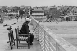 Unknown man sitting on the chair and fishing from the pillar, black and white photo