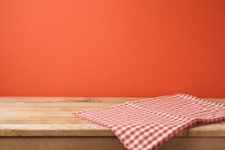 Empty wooden table with red checked tablecloth over red wall  background