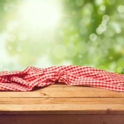 Empty wooden deck table with tablecloth over green bokeh background