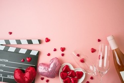 Romantic movie border frame with movie clapper board, heart shapes and wine bottle on pink background. Valentines day concept. Flat lay, top view