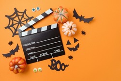 Horror movie night and Halloween party concept with   pumpkin, decorations and movie clapperboard on orange background. Top view, flat lay
