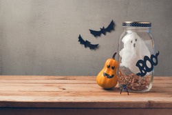 Halloween holiday decoration with ghost in jar and pumpkin with scary face on wooden table