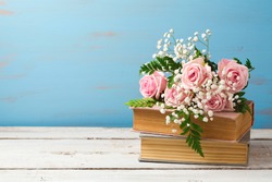 Rose flower bouquet on old books over wooden background with copy space