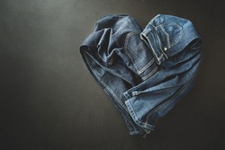 Clothing - heart shape made of two pairs of jeans. Denim trousers captured from above (top view, flat lay). Black chalkboard background with free copy (text) space.