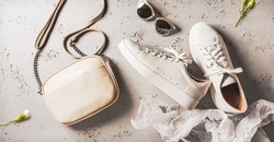 Fashion - spring outfit accessories for woman. White leather sneakers shoes, small beige handbag (purse) and sunglasses on grey background.