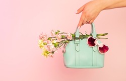 Fashion spring accessories for woman. Small mint green handbag (purse), heart shaped sunglasses and flowers on pastel pink background. Free copy (text) space.