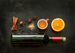 Mulled wine recipe ingredients on black chalkboard with text space - christmas or winter warming drink. Bottle of wine, honey, orange, cinnamon sticks, anise, nutmeg, cloves and sugar from above.