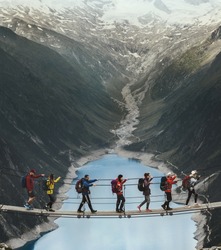 Team of travelers with a backpack in the mountains. A group of travelers crosses a suspension bridge against the backdrop of a mountain and a glacier. Travel and active life concept.