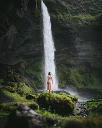 Young and beautiful girl in gentle pink dress looking at the waterfall in Iceland. Iceland waterfall nature travel landscape in Icelandic nature background.