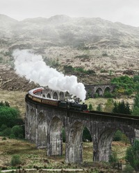 Landscape with viaduct and train. Glenfinnan viaduct in scotland. Retro steam locomotive steam train railway in the mountains.