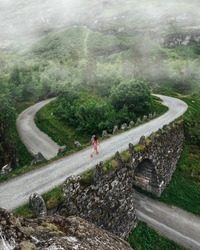 A young girl in a dress runs across a bridge in the mountains of Norway. Road in the mountains with fog. Tourism active life and adventures.