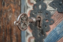 Closeup detail view of old massive metal key in a large huge church wooden ancient door. Secret mystery entrance. Traditional gothic grunge vintage style. Medieval security and safety