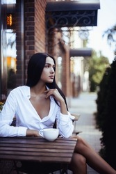Pretty trendy girl drinking coffee in street cafe. Portrait of brunette young model woman. 