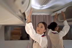 Two woman cabin crews closing the overhead compartment for safety and security check before flight departure. Female flight attendant checking the cabin overhead compartment for safety instruction.