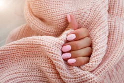 Female hands with beautiful oval-shaped nails, matte pink manicure close-up on a pink knitted sweater background. Shellac. Copy space