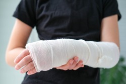 Close-up of a broken arm of a child in a cast. The girl holds her hand bent on the background of a black t-shirt.