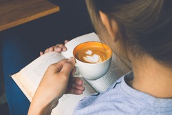 Young woman reading a book and holding cup of coffee
