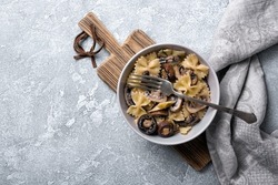 Top view of tasty italian farfalle pasta and champignon mushrooms with cream sauce in bowl on grey concrete background