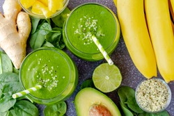 Round glasses filled with green kale and spinach smoothie and green swirled straws surrounded by ingredients