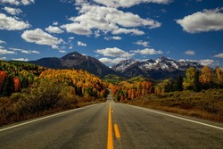 Sunny autumn afternoon scenic drive in the San Juan Mountains near Telluride Colorado with snow covered peaks in distance, yellow and orange Aspen trees near peak fall color - horizontal orientation