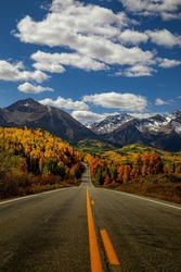 Sunny autumn afternoon scenic drive in the San Juan Mountains near Telluride Colorado along the San Juan Skyway Scenic Byway with snow covered peaks in distance with yellow and orange Aspen trees