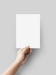 Hand holding blank paper sheet A5 size on grey background.
