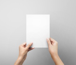 Woman hands holding blank paper sheet A5 size or letter paper on grey background.