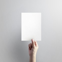 Woman hand holding blank paper sheet A5 size on grey background.