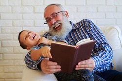 Mid shot of extremely positive grandfather and grandson while reading a funny book. Isolated over white background. Sitting in an armchair