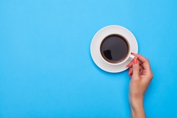 Top view of woman hand holding a cup of coffee over flatlay