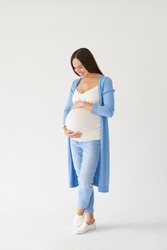 Full-length shot of loving pregnant woman looking at belly while posing in studio 