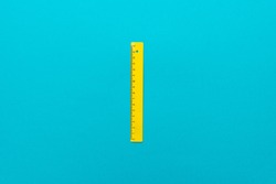 minimalist flat lay photo of yellow plastic ruler on the turquoise blue background. top view of plastic ruler with central composition.
