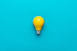 flat lay photo of yellow bulb on turquoise blue backgound. top view of lightbulb in the center of the shot with copy space. minimalist picture of yellow painted electric lamp