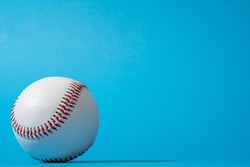 Close-up image of baseball ball on blue background in perspective. Minimalist photo of baseball ball with harsh shadow. Stylish shot of a ball from baseball game with copy space.